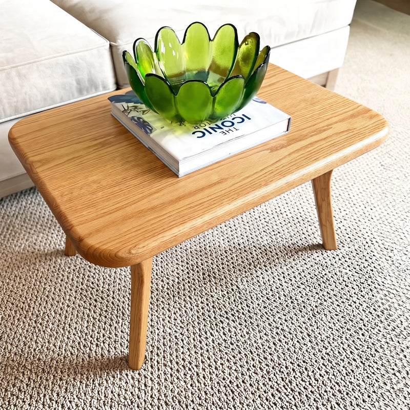 Sidney Rectangular Coffee Table Solid Oak Wood – Mid-Century Modern Design with rounded corners and tapered legs, styled with a green translucent flower-shaped bowl on top of a book in a living room setting.