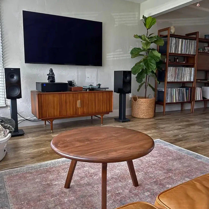 Customer photo showcasing the Sidney Solid Wood Mid-Century Round Coffee Table in a living room setting, harmoniously placed among other wooden furniture, with a TV unit visible in the background, highlighting its cohesive design.