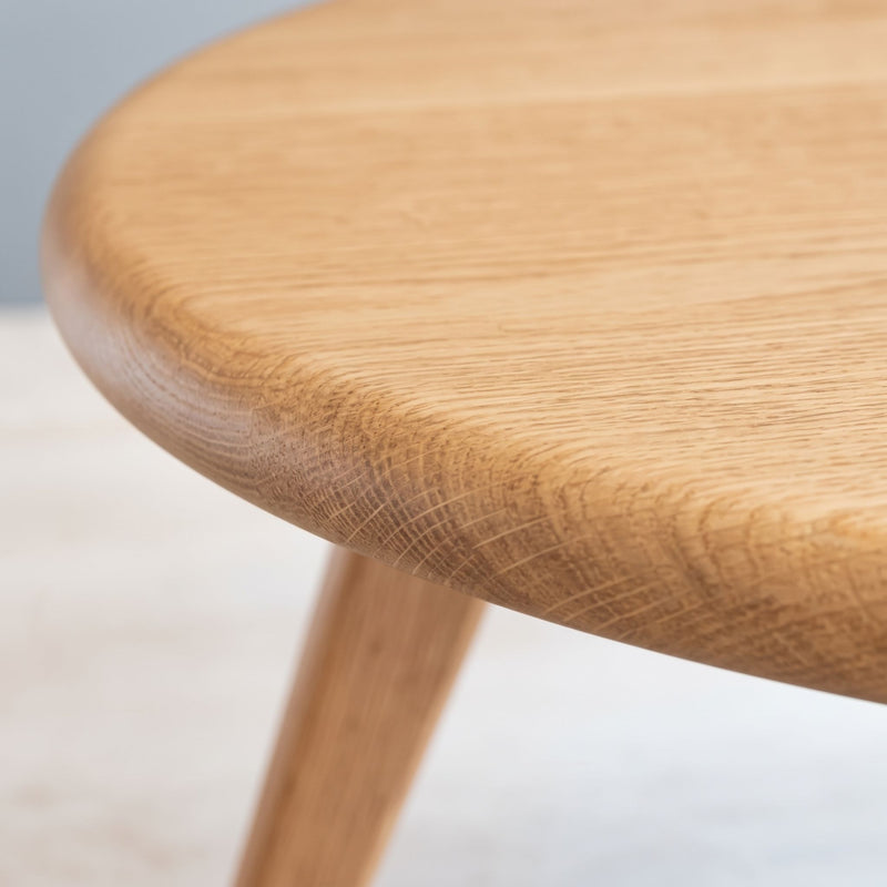 Close-up of Sidney Solid Oak Wood Round Coffee Table showing the rounded edge of the circular tabletop and part of the tapered wooden leg.