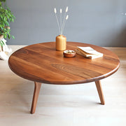 High-angle view of the Sidney Solid Wood Mid-Century Round Coffee Table, showcasing the elegant walnut wood grain, rounded edges, and robust mid-century legs, complemented by tasteful decor items on the surface.