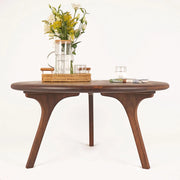 Direct front view of the Sidney Solid Wood Mid-Century Round Coffee Table on a white background, captured from a lower angle. The aesthetic, sturdy wooden legs and rich walnut wood grain are showcased, with elegant decor items arranged on the tabletop.