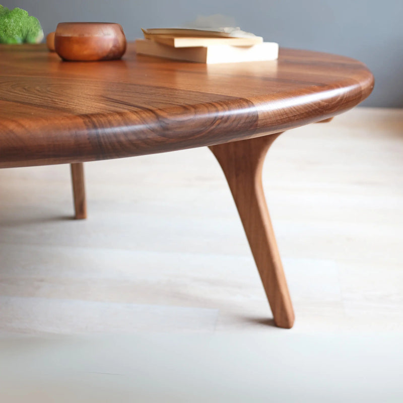 Close-up view of the Sidney Solid Wood Mid-Century Modern Round Coffee Table, emphasizing the rich walnut wood grain, smooth rounded edges, and intricate details of the sturdy legs, showcasing its quality craftsmanship.