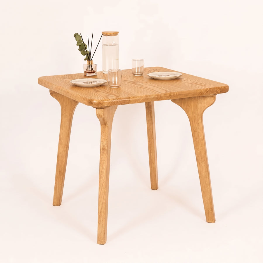 Sidney Square Dining Table Solid Oak Wood – Mid-Century Modern Design with four tapered legs and a square top, styled with a glass carafe, drinking glasses, and small plates on a clean white background.