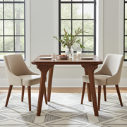 Sidney Square Dining Table | Walnut Wood Mid Century Design and two upholstered chairs in a bright dining room with large windows and a geometric rug.