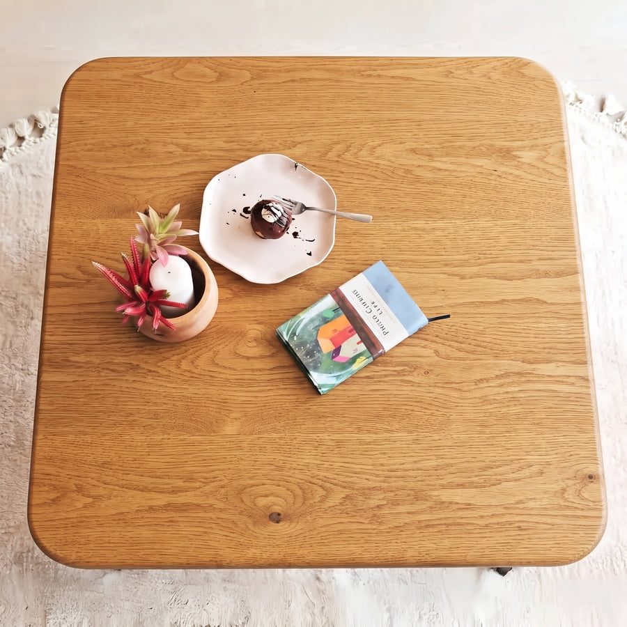 Sidney Square Wood Coffee Table Solid Oak Wood – Mid-Century Modern Design with rounded corners, styled with a small potted succulent, a plate with a chocolate dessert, and a book on a white textured rug.