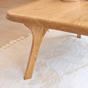 Close-up of Sidney Square Wood Coffee Table Solid Oak Wood – Mid-Century Modern Design corner with a curved apron and tapered legs, resting on a white textured rug.