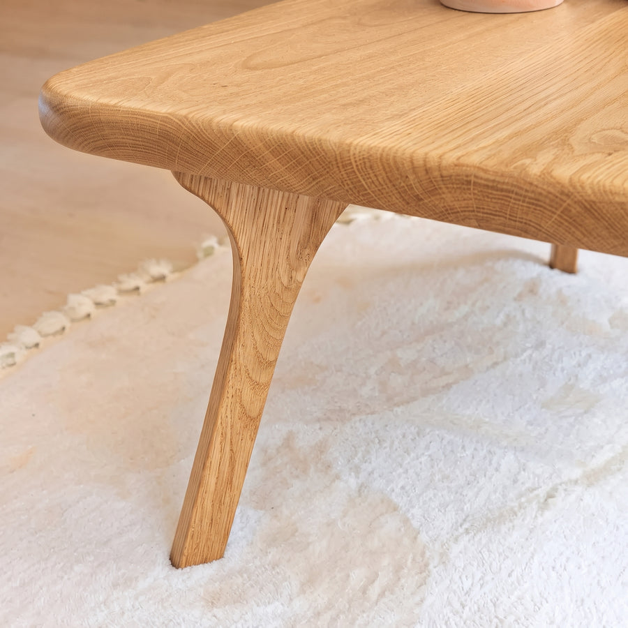 Close-up of Sidney Square Wood Coffee Table Solid Oak Wood – Mid-Century Modern Design corner with a curved apron and tapered legs, resting on a white textured rug.