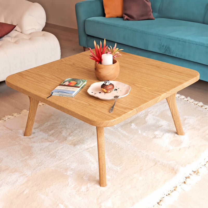 Sidney Square Wood Coffee Table Solid Oak Wood – Mid-Century Modern Design with tapered legs, styled in a cozy living room setting with a plush cream rug, a teal sofa, and decorative items on top.