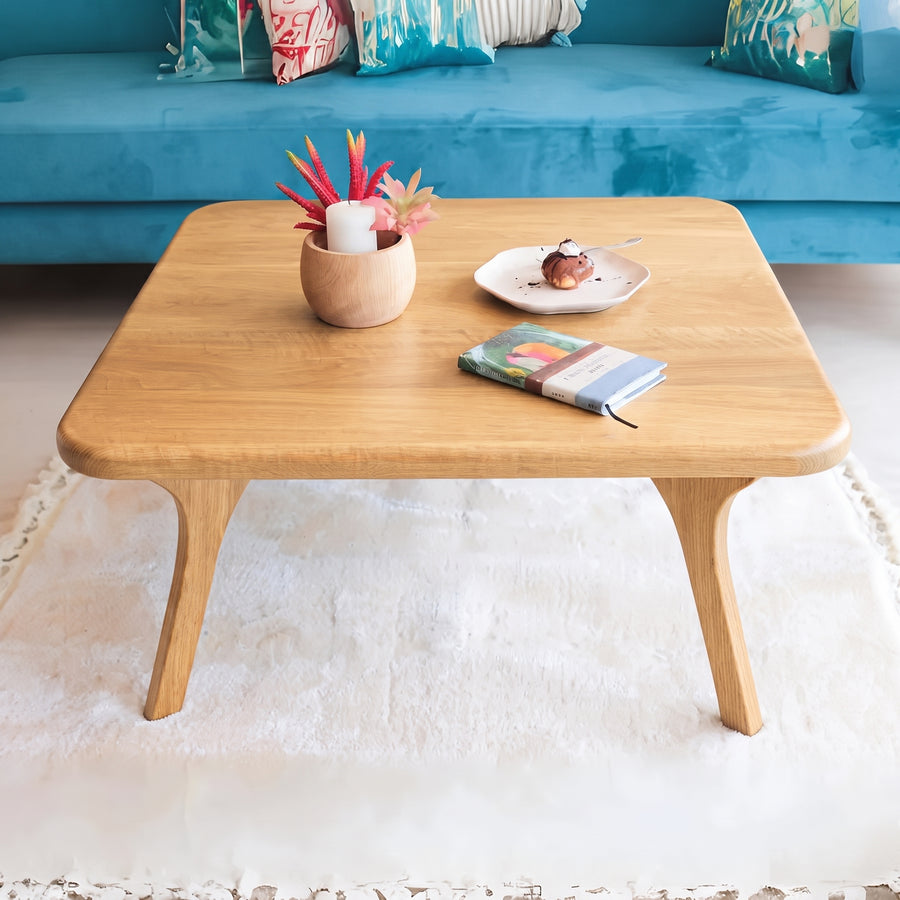 Sidney Square Wood Coffee Table Solid Oak Wood – Mid-Century Modern Design with rounded corners and angled legs, styled in a living room setting with a blue sofa, white rug, and small decorative items on top.