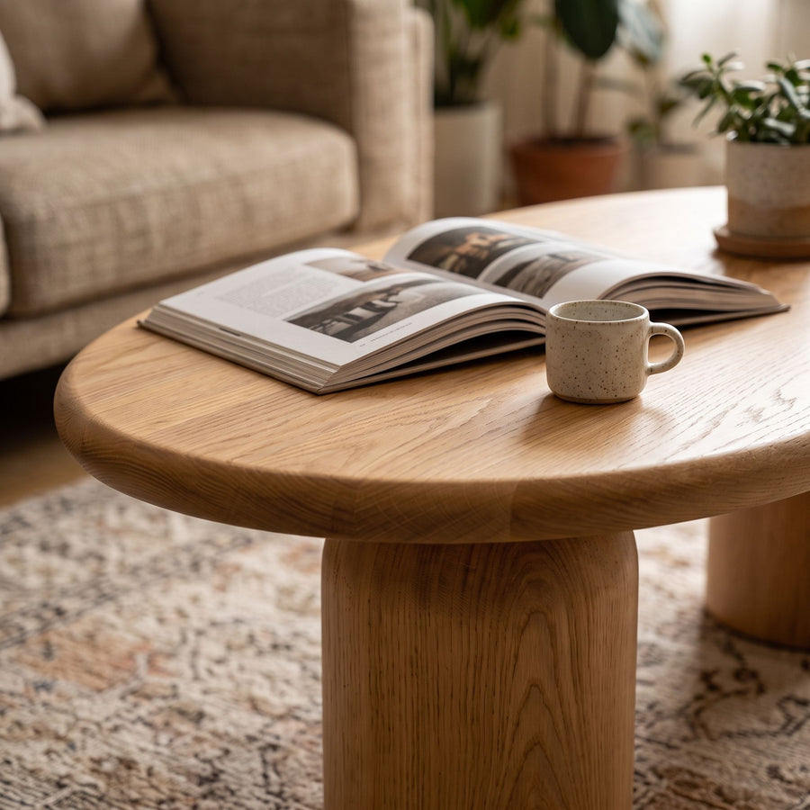 Close-up view of the Solen Oval Solid Wood Coffee Table – Oak & Walnut Sculptural Double Pedestal Design in a natural oak finish, decorated with a book and a coffee mug.