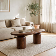 The Solen Oval Solid Wood Coffee Table – Oak & Walnut Sculptural Double Pedestal Design in a walnut finish styled in a bright, modern living room setup.