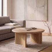 Soren Round Oak Coffee Table | Sculptural Scandinavian Modern Design with chunky block legs in a modern living room setting next to a gray sofa.