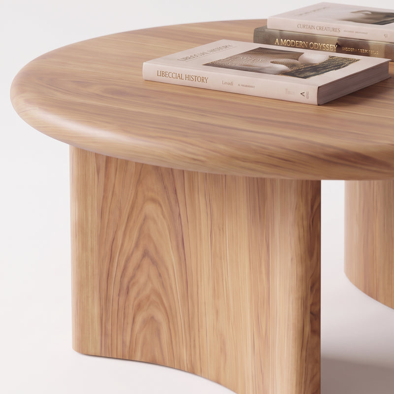 A close-up of Soren Round Oak Coffee Table | Sculptural Scandinavian Modern Design with a thick, sculptural pedestal base and a warm natural wood grain finish. Two books are placed on top of the table against a clean white background.