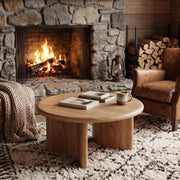 Soren Round Oak Coffee Table | Sculptural Scandinavian Modern Design in a cozy living room setting with a stone fireplace, leather armchair, and shag rug.