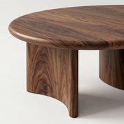 A close-up of Soren Round Solid Walnut Coffee Table with a rich dark brown walnut grain finish and sculptural curved legs, set against a clean off-white background.