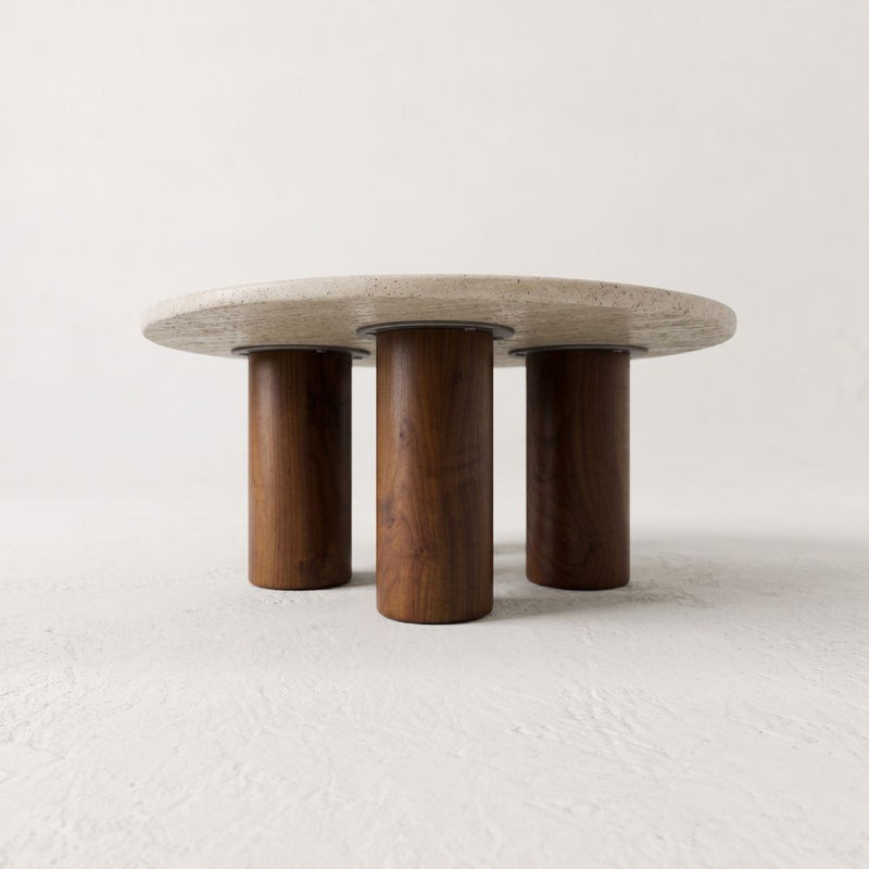 Low-Angle Studio View of Terra Round Travertine Coffee Table with Walnut Wood Triple Pedestal Base - Sculptural Modern Design by Tomruque