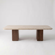 Eye-level straight-on studio shot of Wilder Rectangular Travertine Coffee Table featuring a rounded-corner beige stone top and dual solid walnut column bases