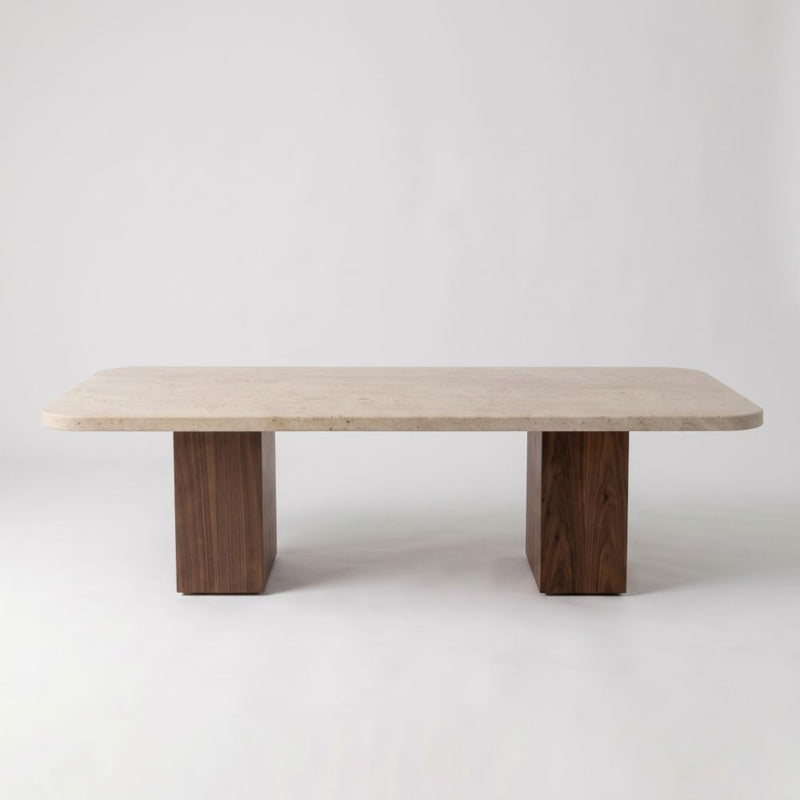 Eye-level straight-on studio shot of Wilder Rectangular Travertine Coffee Table featuring a rounded-corner beige stone top and dual solid walnut column bases