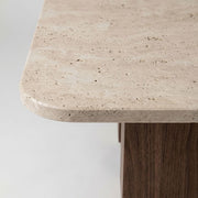 Detailed studio close-up showing porous beige travertine stone top edge, rounded corner, and solid walnut column base on Wilder Rectangular Coffee Table