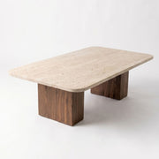 Three-quarter studio view of Wilder Rectangular Travertine Coffee Table featuring a rounded-corner beige stone top and dual solid walnut column bases