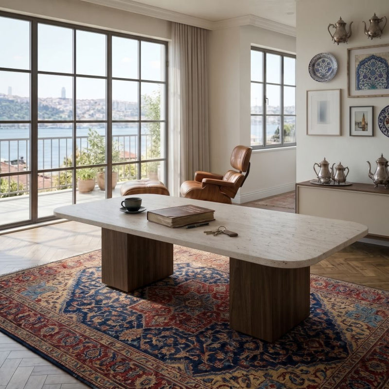 Wilder Rectangular Travertine Coffee Table with Solid Walnut Column Bases Styled on Oriental Rug with Leather Lounge Chair and Sea View Window in Luxury Living Room