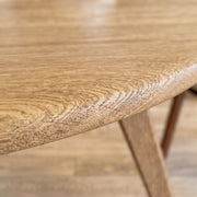 Close-up of Sidney Circular Dining Table Solid Oak Wood – Mid-Century Modern Design showing the natural wood grain and rounded edge, with part of the wooden leg visible against a matching wood floor.
