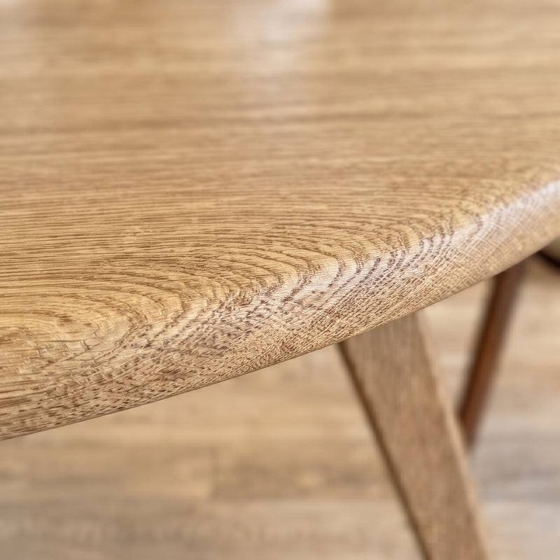Close-up of Sidney Circular Dining Table Solid Oak Wood – Mid-Century Modern Design showing the natural wood grain and rounded edge, with part of the wooden leg visible against a matching wood floor.