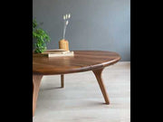 Product video of the Sidney Solid Wood Mid-Century Round Coffee Table, highlighting its rich walnut wood grain, smooth rounded edges, and sturdy aesthetic legs. Captured from various angles, stylish decor items enhance its modern mid-century appeal.